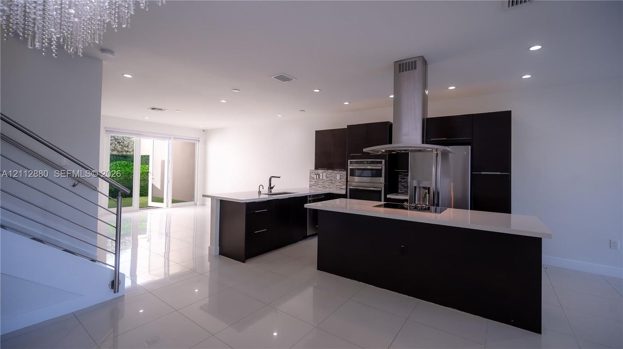 Kitchen featuring dark cabinetry, quartz countertops, a stainless steel range hood, built-in wall oven, and polished tile flooring