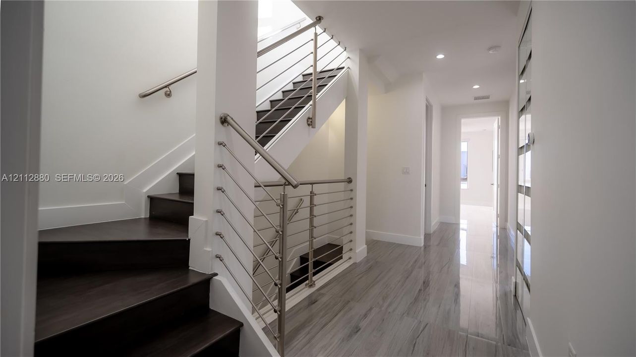 Staircase featuring dark wood-finish treads, a metal tension-cable railing, and a minimalist handrail, complemented by large-format tile flooring and recessed lighting