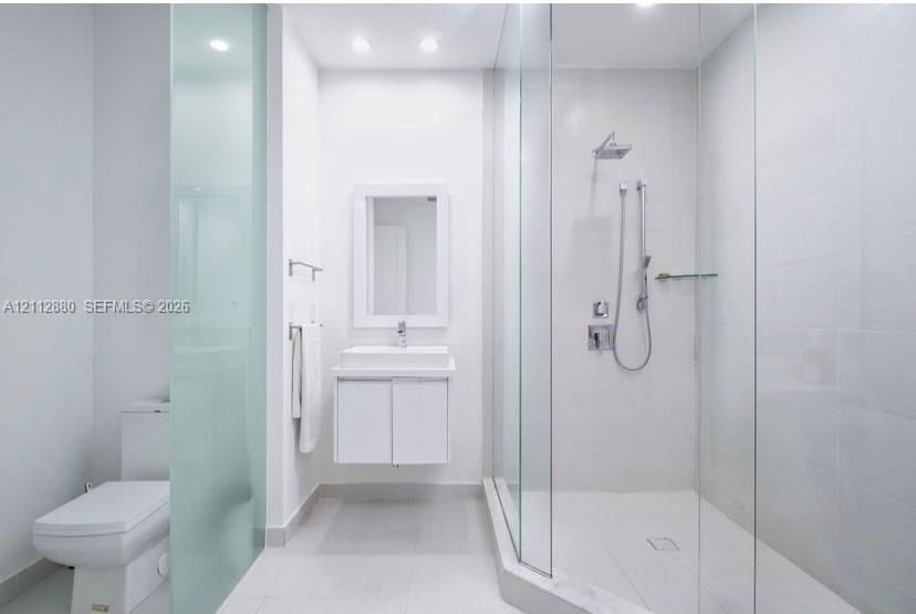 Bathroom featuring a glass-enclosed shower with a rainfall showerhead and handheld sprayer, a floating vanity with a rectangular sink, a recessed wall mirror, and floor-to-ceiling frosted glass privacy panels