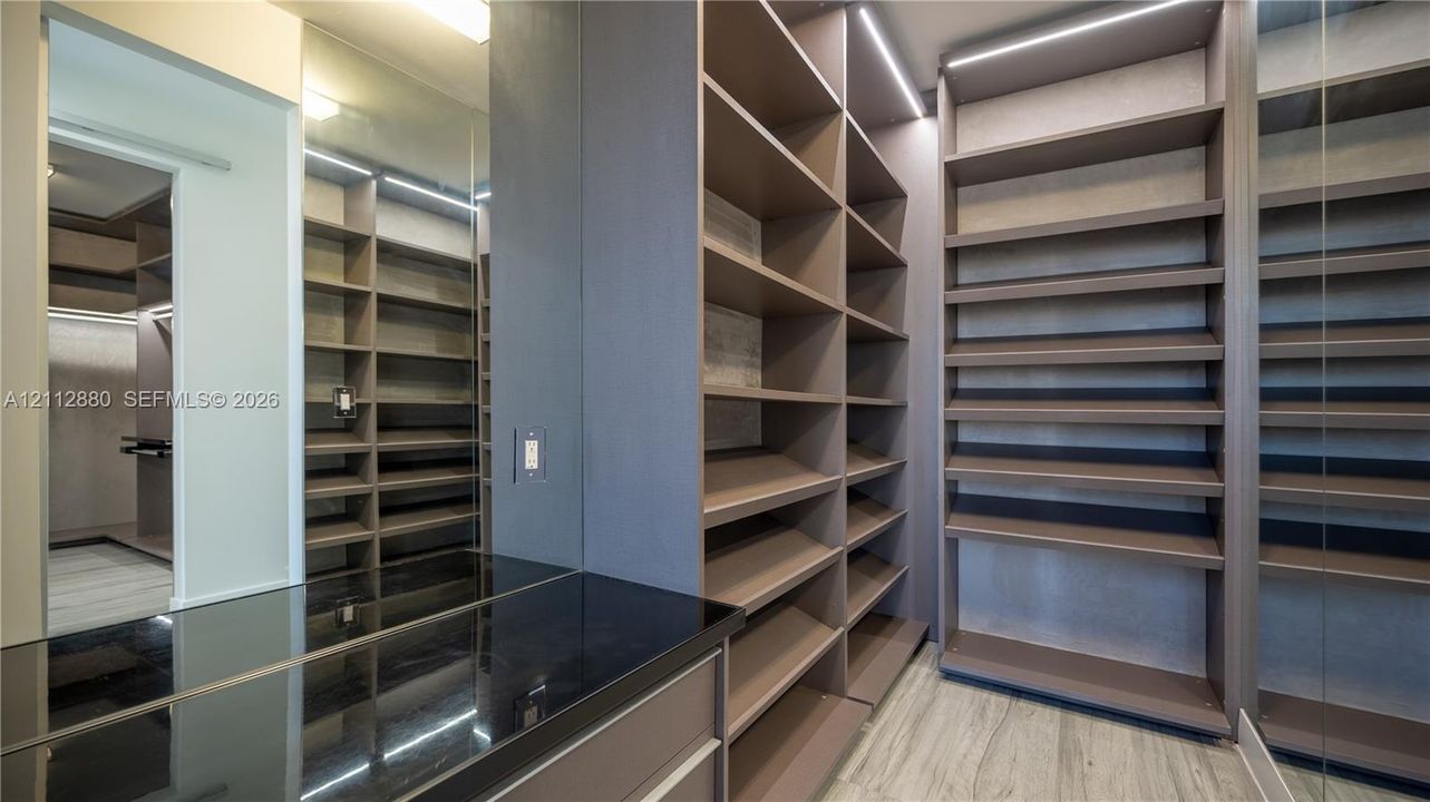 Custom walk-in closet featuring extensive built-in shelving, integrated strip lighting, full-length mirror panels, a dark-toned countertop,