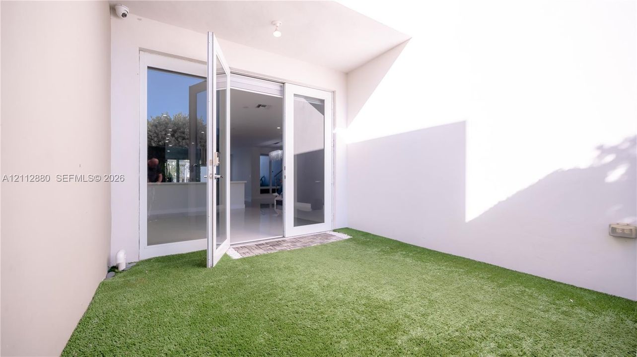Enclosed patio featuring synthetic turf, high privacy walls, and double-glass entry doors