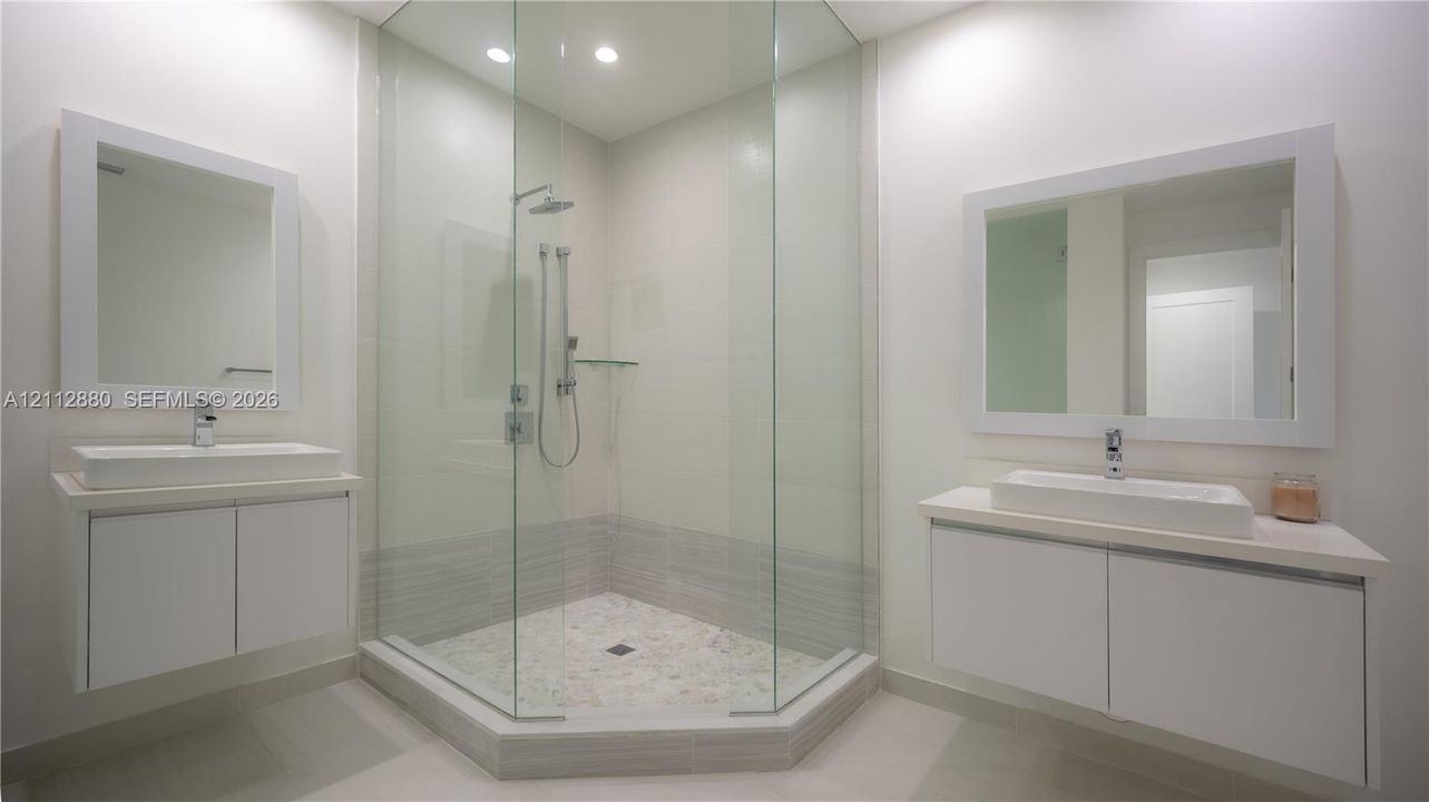 Dual floating vanities featuring rectangular vessel sinks and white cabinetry, paired with a glass-enclosed shower with polished chrome fixtures and tile flooring