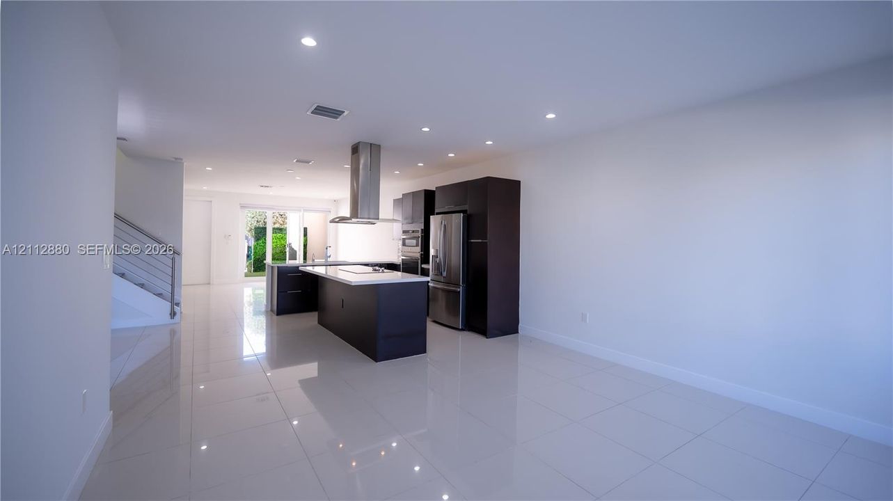 Modern kitchen featuring dark cabinetry, a central island with a stone-finish countertop, recessed lighting, polished tile flooring, and a stainless steel vent hood