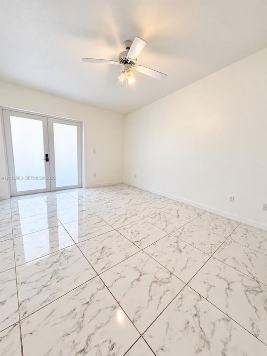 Glossy large-format tile flooring, double glass panel exterior doors, and a ceiling-mounted fan with integrated light fixture