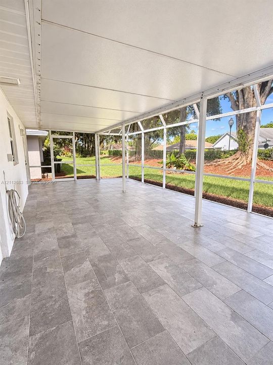 Screened-in patio featuring a solid roof, large-format grey tile flooring, and expansive metal-framed screening