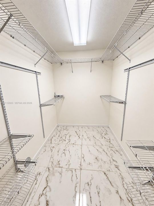 Storage space featuring stone-patterned tile flooring, multi-level wire shelving, and overhead linear lighting