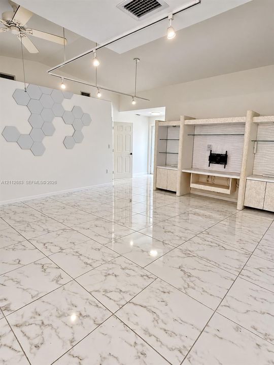 Polished stone-finish tile flooring, custom built-in cabinetry with glass shelving, geometric wall paneling, and adjustable track lighting