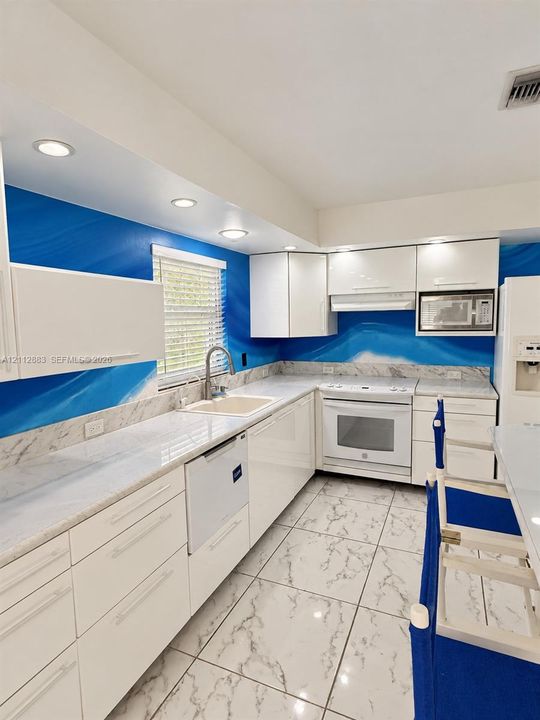 Kitchen featuring flat-panel white cabinetry, stone-surface countertops, integrated under-mount sink, recessed lighting, and large-format tile flooring