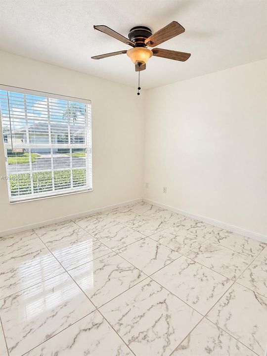 Large-format tile flooring with a veined finish, multi-pane window with integrated horizontal blinds, and a five-blade ceiling fan featuring a central light fixture