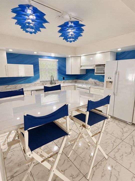 Kitchen featuring high-gloss cabinetry, stone-finish countertops, tile flooring, two decorative pendant lights, and a built-in microwave
