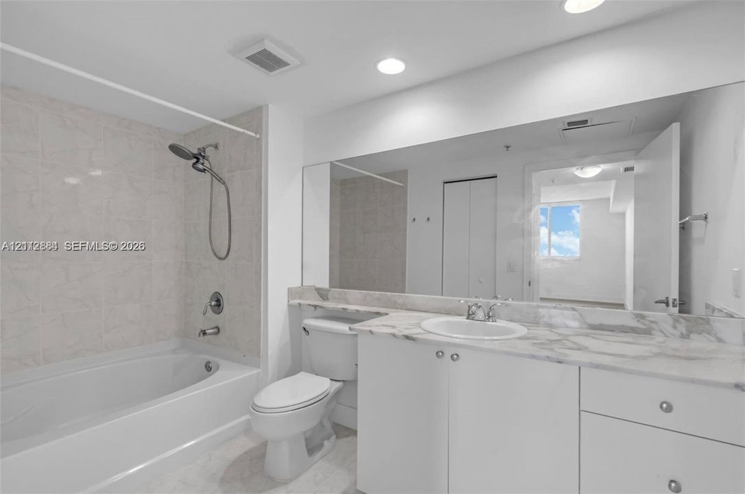 Bathroom featuring a white vanity with stone-finish countertop, undermount sink, full-width wall mirror, and a tub with tiled surround and handheld shower fixture