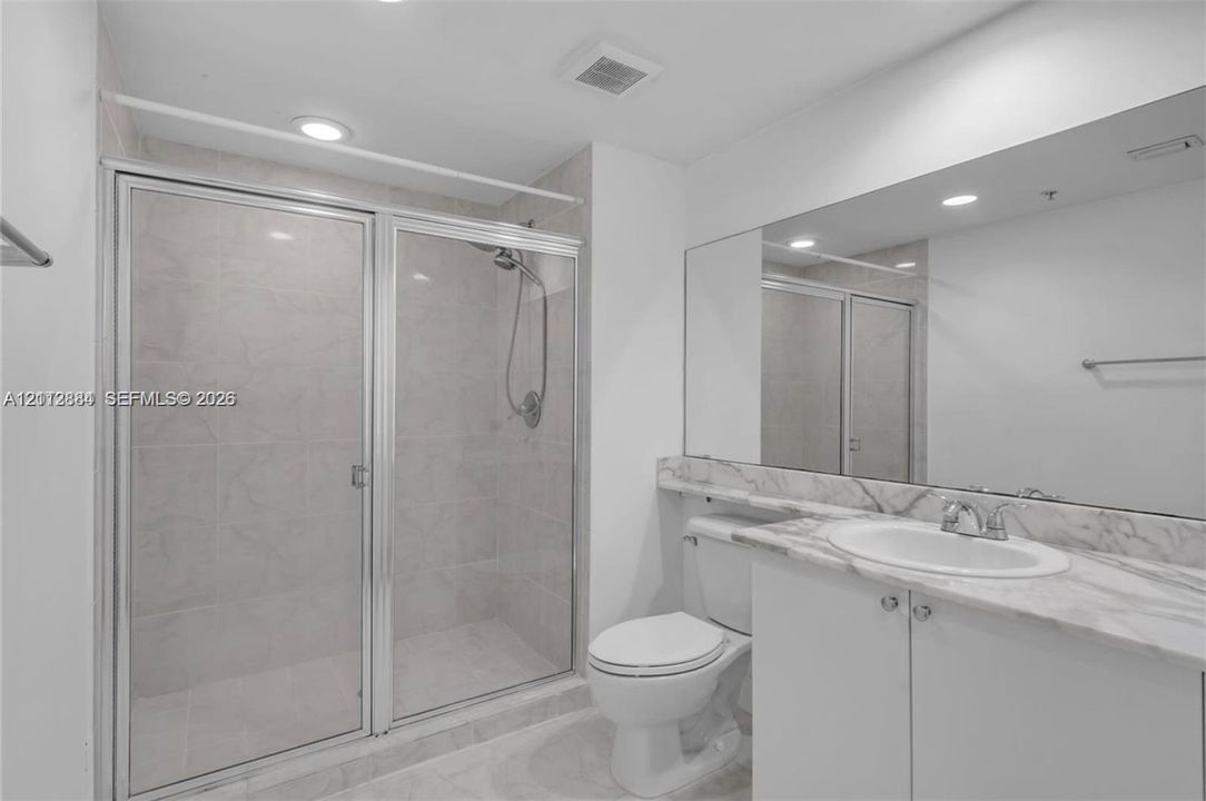 Bathroom featuring a walk-in shower with glass enclosure, stone-finish countertop, undermount sink, and full-width vanity mirror