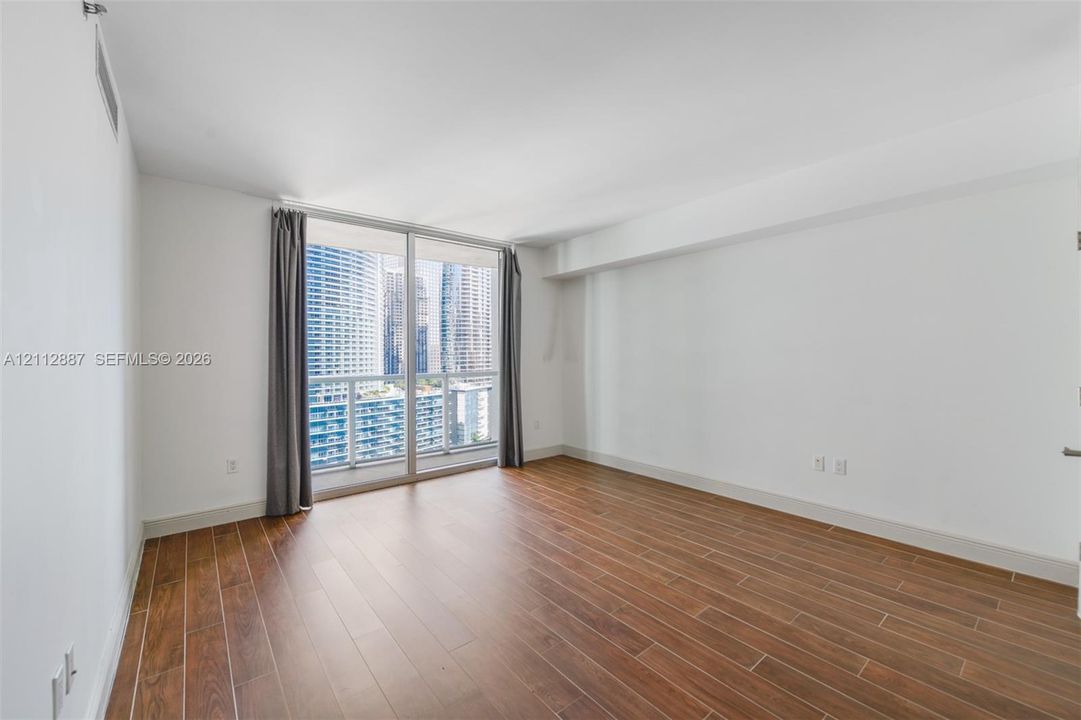 Living area featuring wood-finish flooring, floor-to-ceiling glass sliding doors, and a glass-paneled balcony