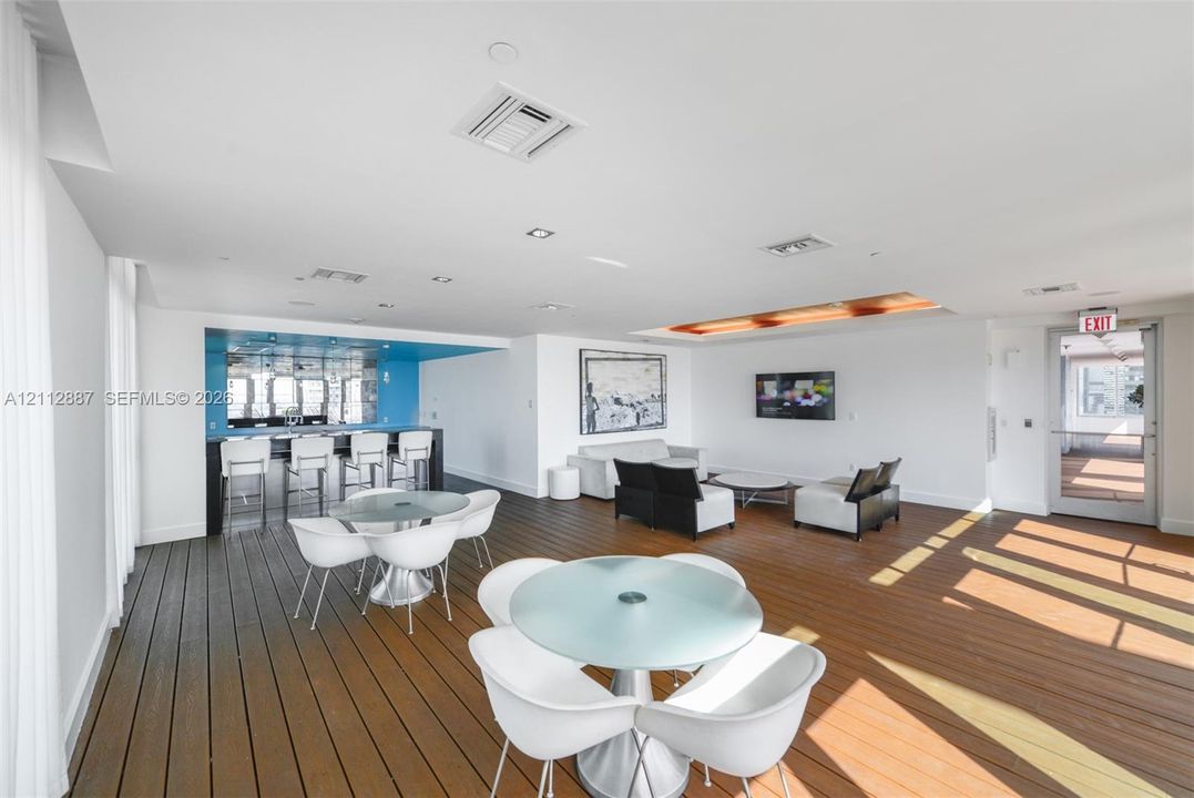 Open-concept interior featuring wood-finish flooring, a built-in bar with blue accent wall, recessed lighting, and a tray ceiling with integrated illumination