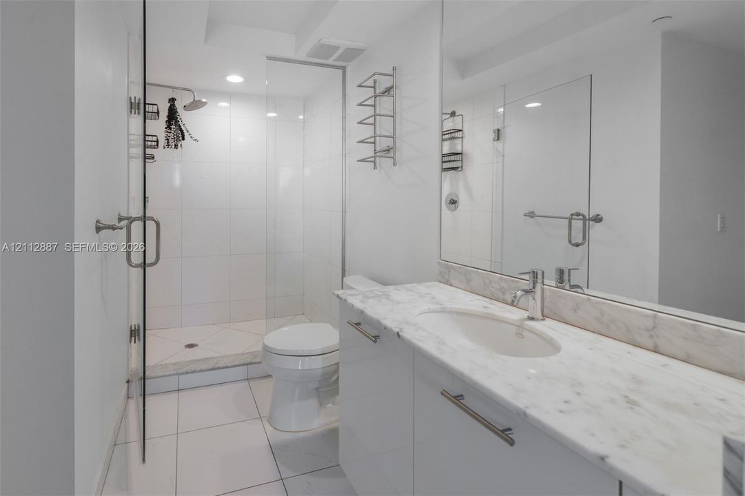 Bathroom featuring a glass-enclosed walk-in shower with white wall tile, a vanity with a white countertop and undermount sink, a large wall-to-wall mirror, and oversized tile flooring