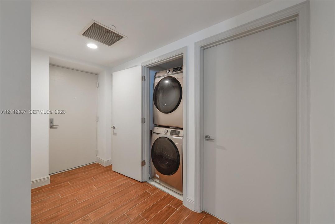 Utility area featuring wood-finish flooring, stackable front-load laundry appliances, and smooth-finish interior doors with metallic hardware