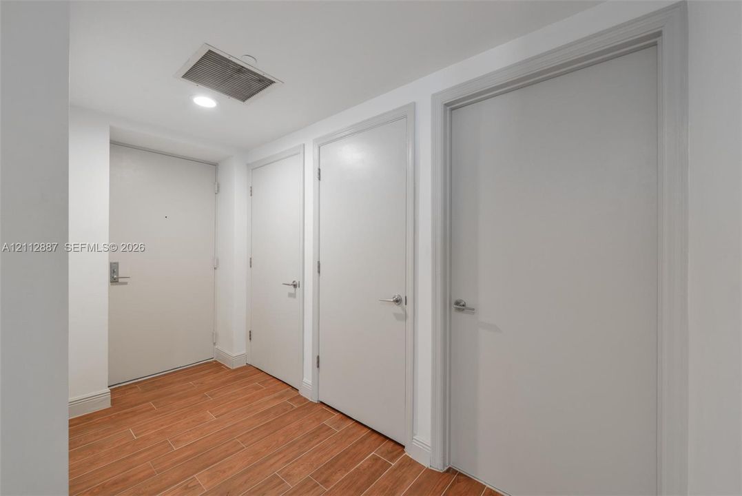Interior hallway featuring wood-finish tile flooring, recessed lighting, and three solid-core interior doors with satin nickel hardware