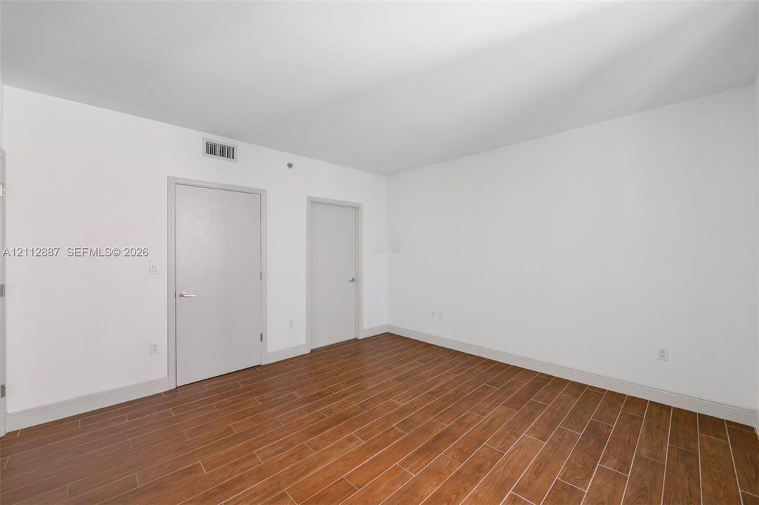 Interior room featuring wood-finish tile flooring, neutral wall paint, and two interior doors with metallic lever handles