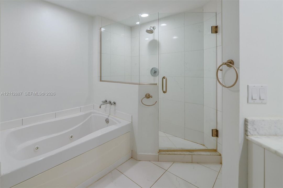 Bathroom featuring a jetted soaking tub with wall-mounted faucet, a walk-in shower with glass enclosure, large-format tile surround, and stone-topped vanity