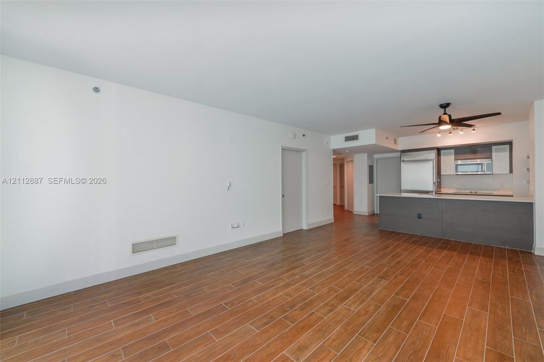Open-concept interior featuring wood-finish flooring, a kitchen island with stone-surface countertop, cabinetry with integrated microwave, and a ceiling-mounted light fixture