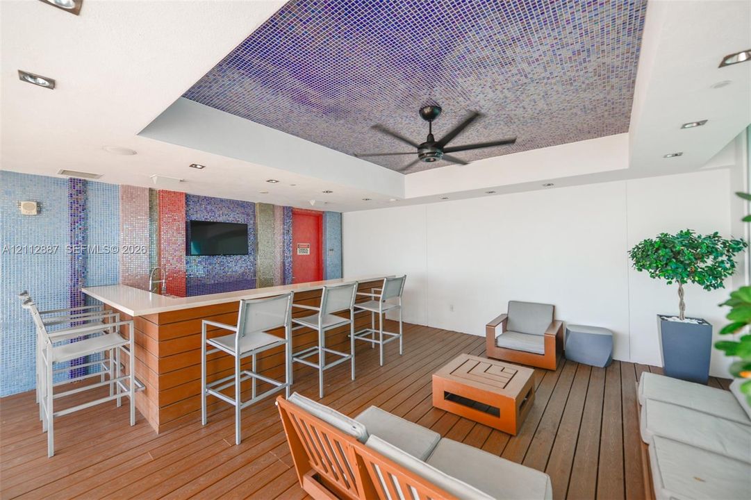 Outdoor bar area featuring a mosaic tile accent wall and ceiling inlay, composite wood-finish decking, integrated bar sink, and recessed ceiling lighting