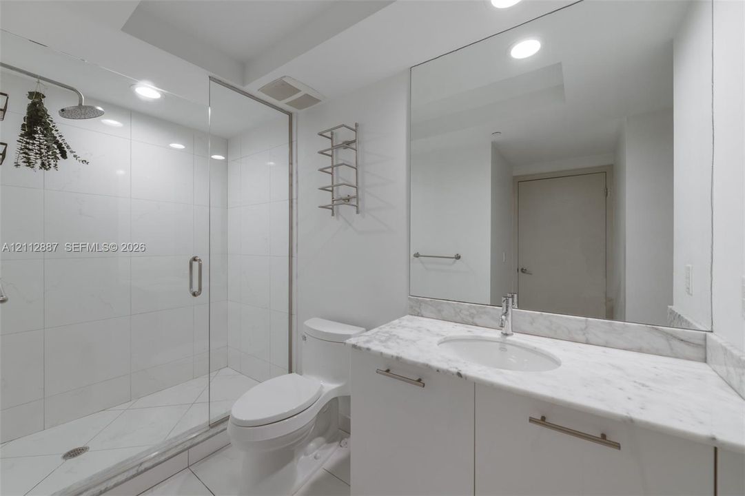 Bathroom featuring a glass-enclosed shower with tiled walls, stone-top vanity with an undermount sink, large wall-to-wall mirror, and recessed lighting