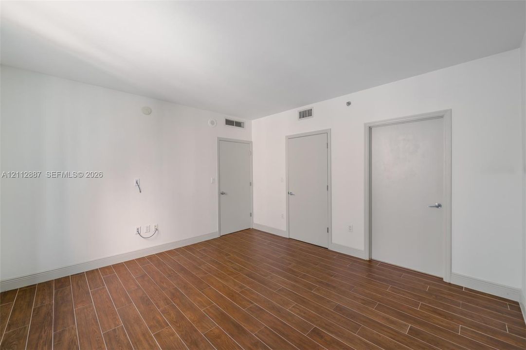 Interior space featuring wood-finish flooring, smooth walls, and three solid-core interior doors with metallic hardware