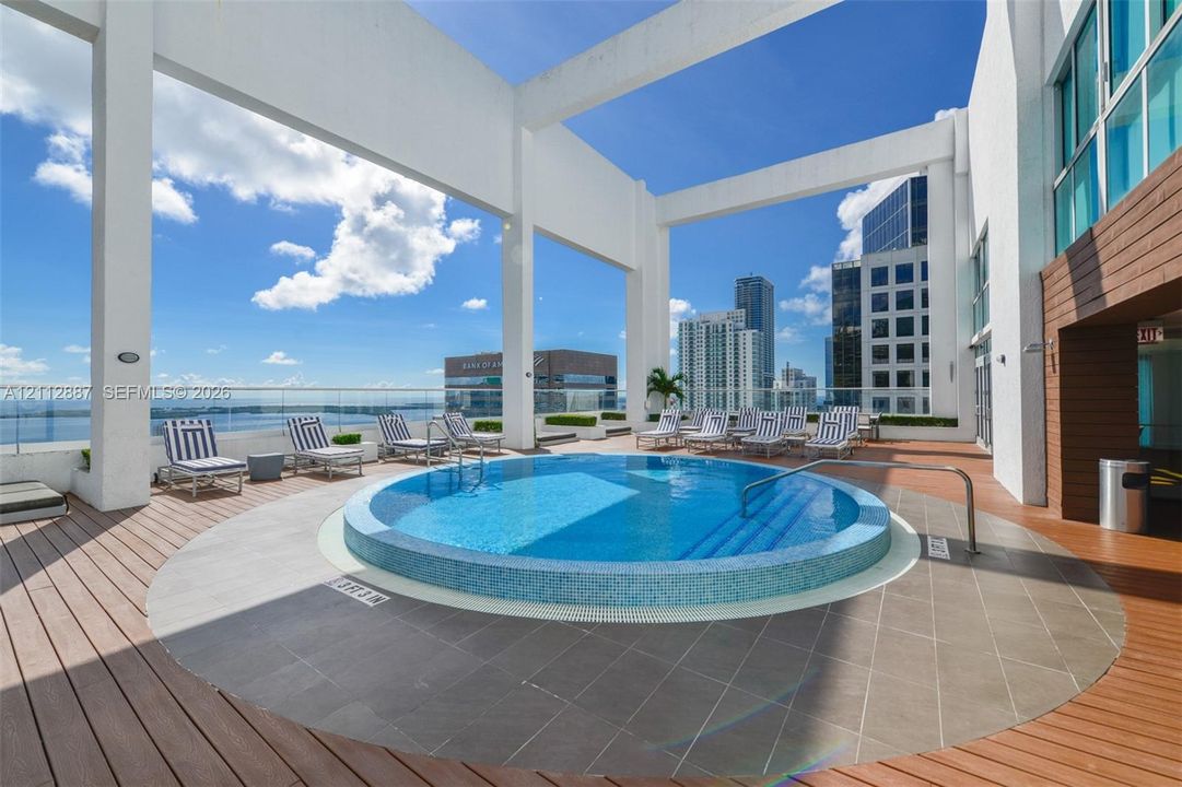Rooftop pool with circular basin and tile surround, set within a covered deck featuring wood-finish flooring and glass panel railings
