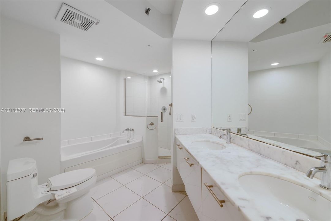 Dual-sink vanity with a stone countertop, built-in soaking tub, glass-enclosed shower, and large wall-mounted mirror