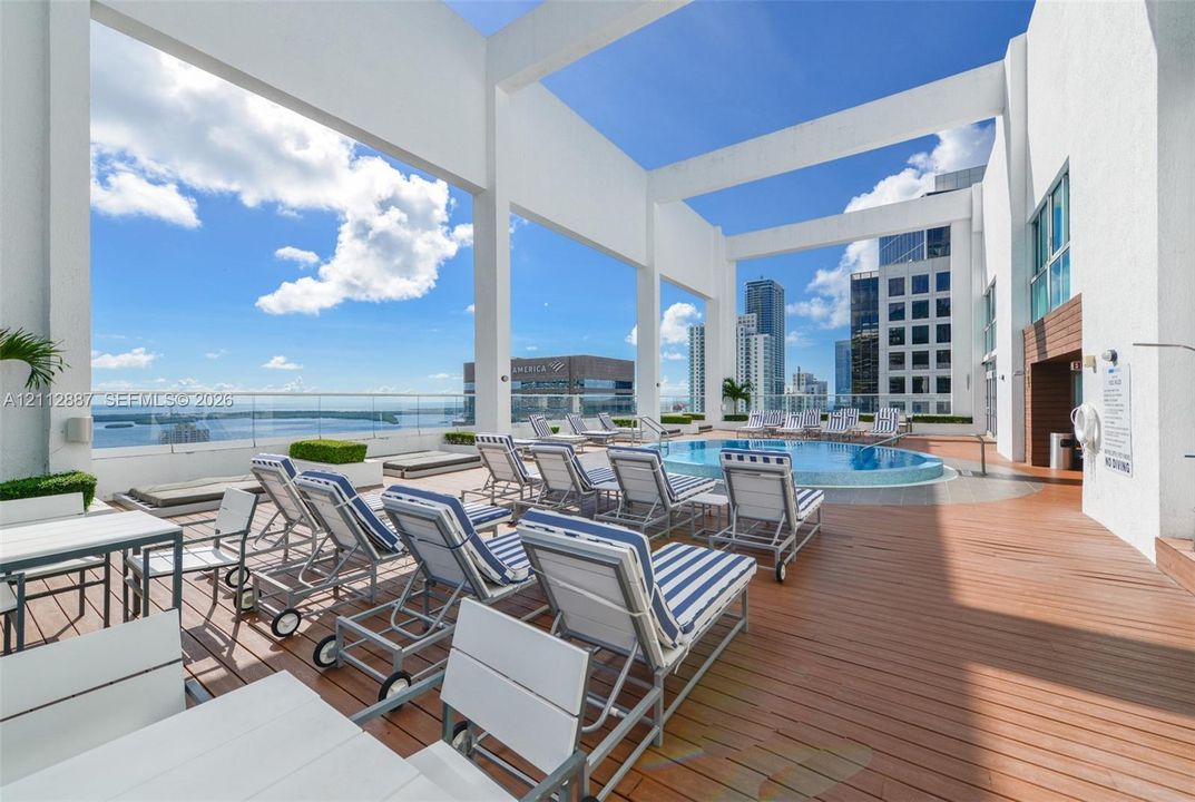 Rooftop terrace featuring wood-finish decking, circular swimming pool, glass railing, and concrete structural columns