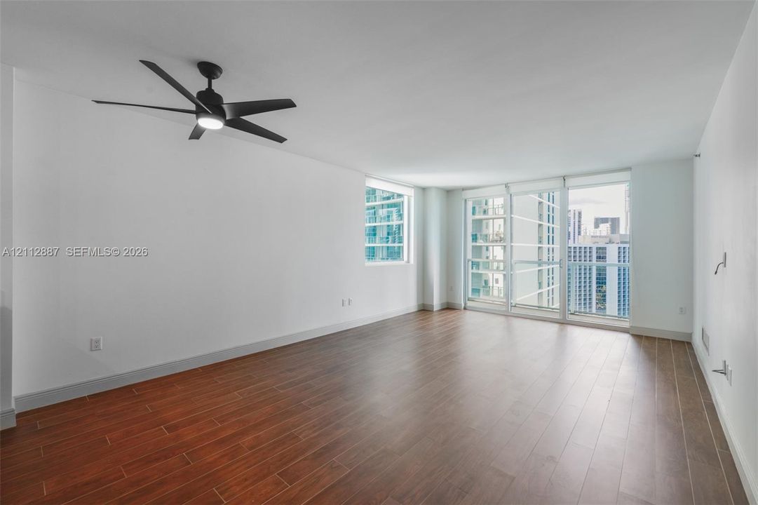 Interior featuring wood-finish flooring, floor-to-ceiling windows, sliding glass door with a glass panel railing, and a matte black ceiling fan with an integrated light fixture