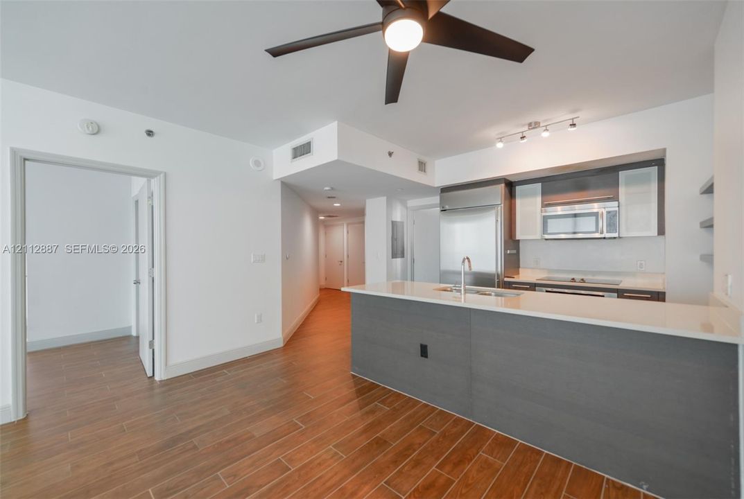 Kitchen featuring an integrated stainless steel refrigerator, stone-surface breakfast bar, wood-finish flooring, and a modern ceiling fan with integrated lighting