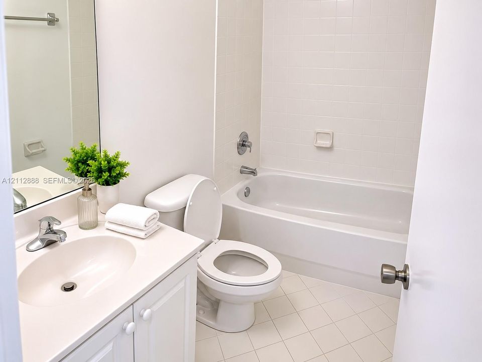 Bathroom featuring a white vanity cabinet with an integrated sink, polished metal faucet, white tile tub surround, and porcelain tile flooring