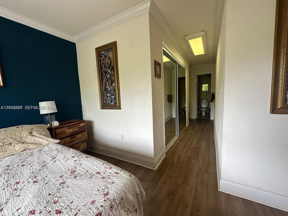 Wood-finish flooring, sliding mirror-panel closet doors, crown molding, and recessed rectangular lighting