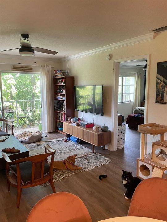 Wood-finish flooring, ceiling fan, and glass sliding door providing outdoor access to a balcony with metal railing