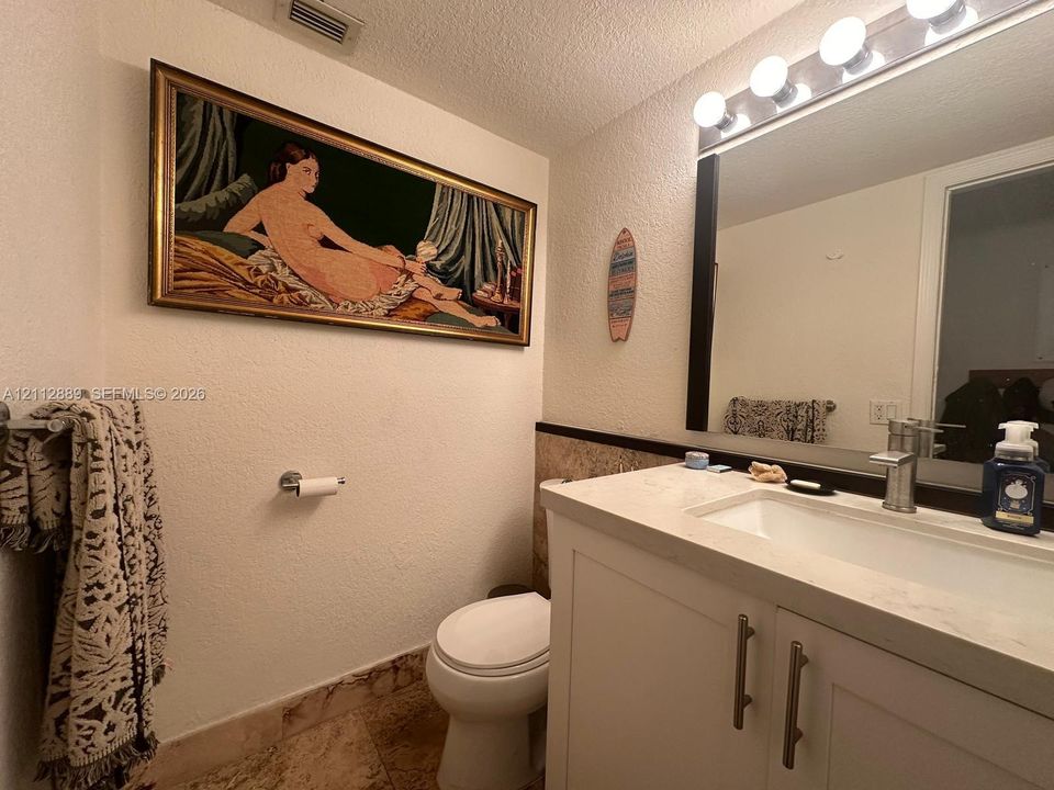 White vanity cabinet with integrated rectangular sink and stone countertop, polished metal faucet, full-width mirror with integrated five-bulb lighting, and stone flooring