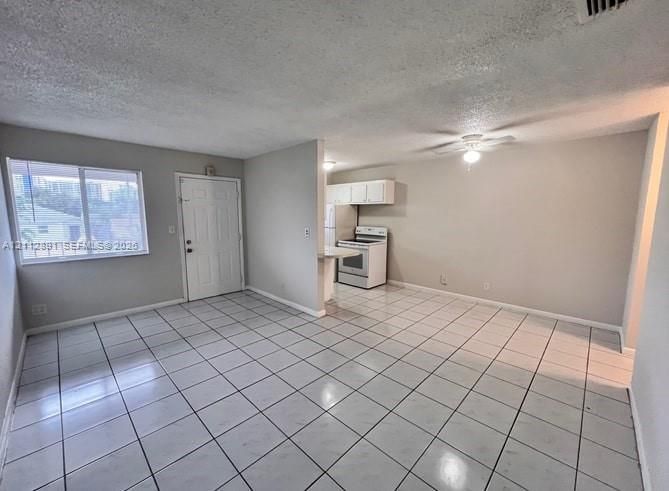 Open-concept area featuring white ceramic tile flooring, a ceiling-mounted light fixture, a large window, and an eat-in kitchen area with white cabinetry