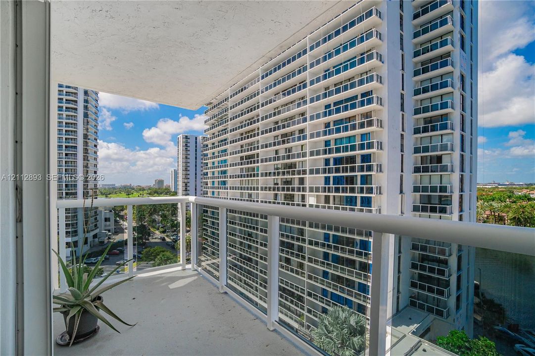 Covered balcony featuring concrete flooring and a white powder-coated metal railing with glass panels