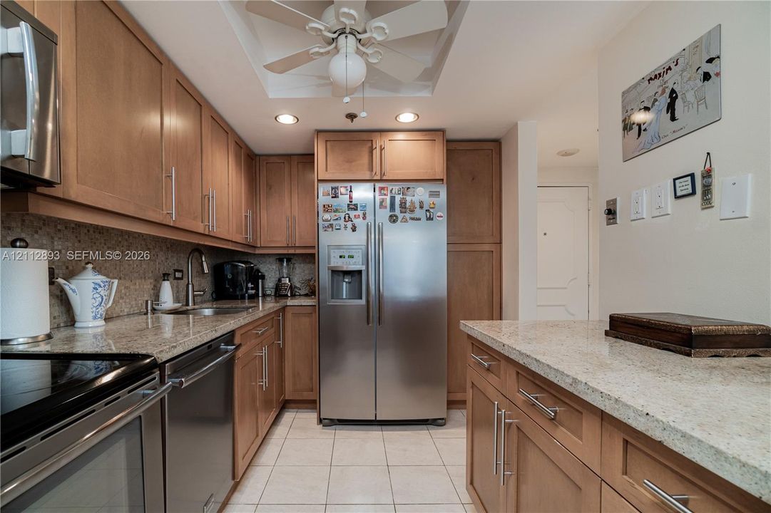 Kitchen featuring natural wood cabinetry, stone-finish countertops, stainless steel appliances, tiled flooring, and recessed ceiling lighting