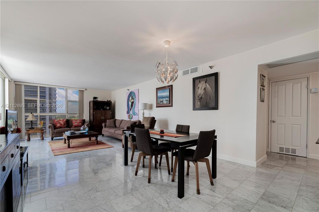 Open-concept interior featuring light-toned stone flooring, floor-to-ceiling windows, and a spherical multi-light pendant fixture