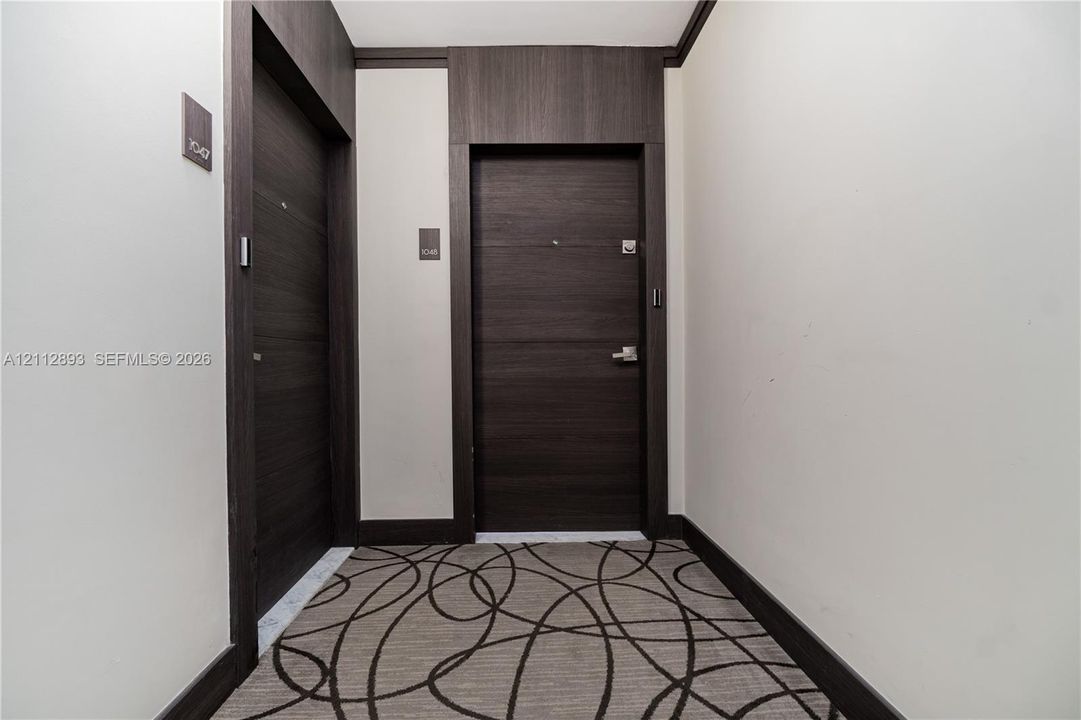 Entryway featuring two dark wood-finish doors with brushed metal hardware, high-contrast dark wood-finish door casing and trim, and patterned wall-to-wall carpeting