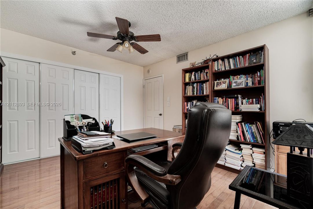 Wood-finish flooring, built-in shelving, triple-panel closet doors, and ceiling fan with integrated lighting