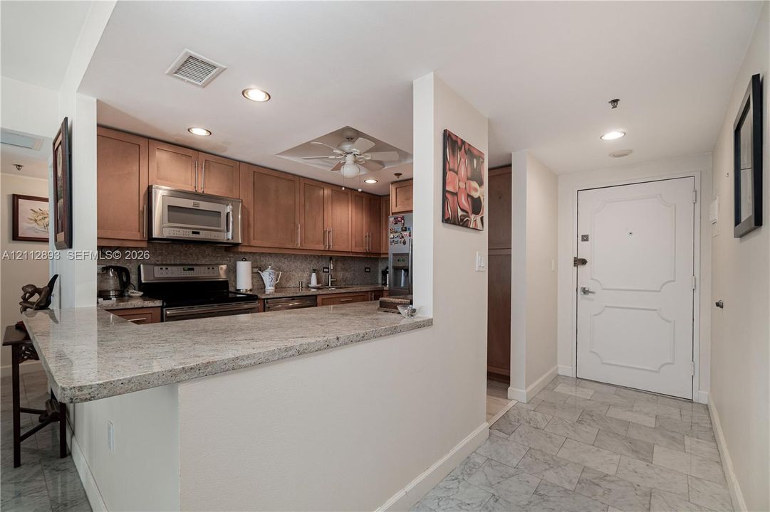 Kitchen featuring light-finish cabinetry, stone countertops, stainless steel appliances, a recessed ceiling fan, and stone tile flooring