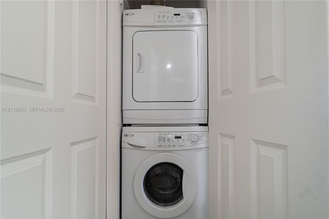 Stackable laundry unit featuring a white front-loading washing machine and a matching dryer, enclosed by white paneled closet doors