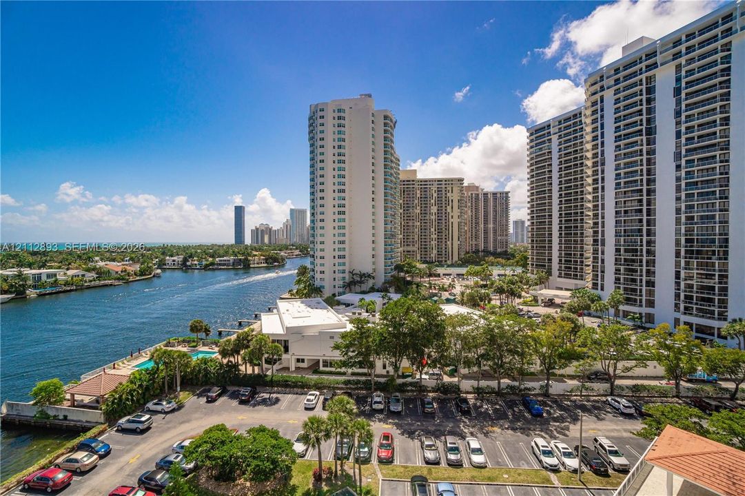 High-rise vantage point featuring a waterway, mature palm trees, paved parking area, and coastal landscape