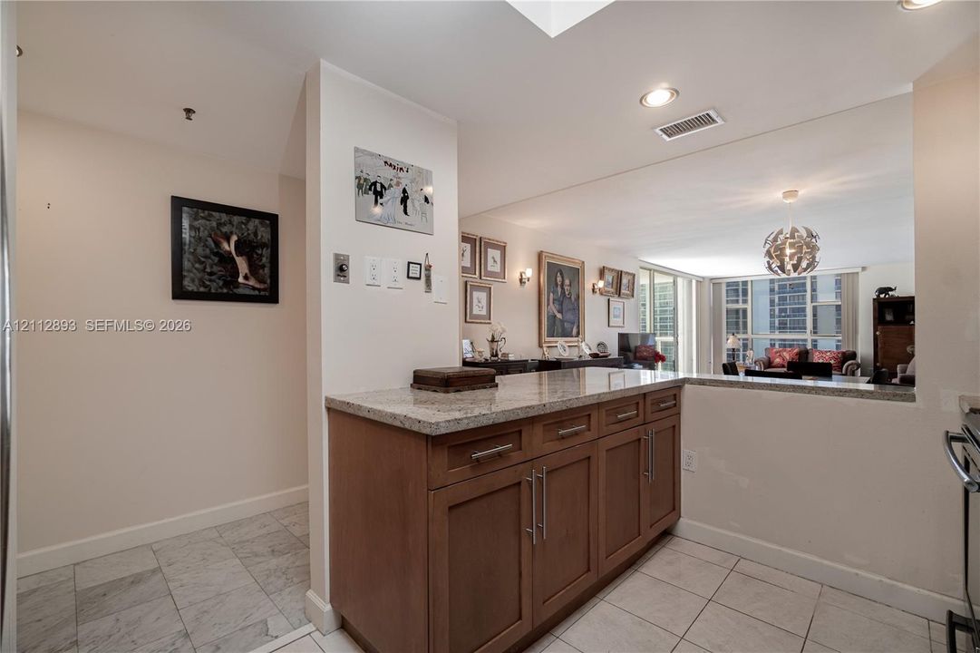 Kitchen area featuring wooden cabinetry with stainless steel bar pulls, stone-composite countertops, recessed lighting, and tile flooring