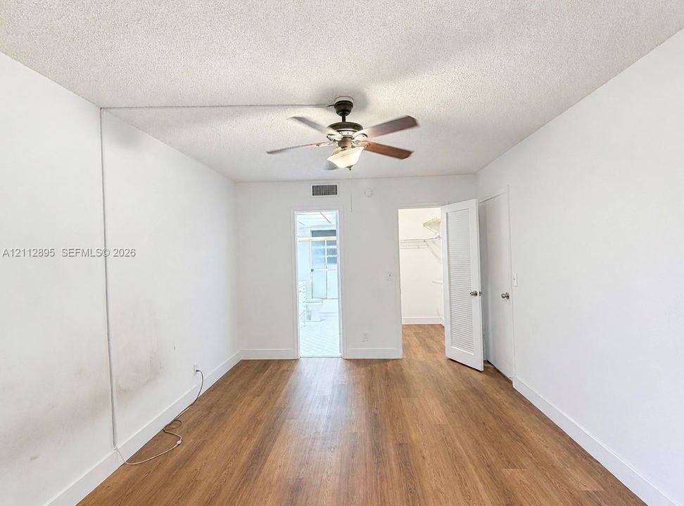 Room featuring wood-finish flooring, a ceiling fan with integrated lighting, and a walk-in closet with built-in shelving