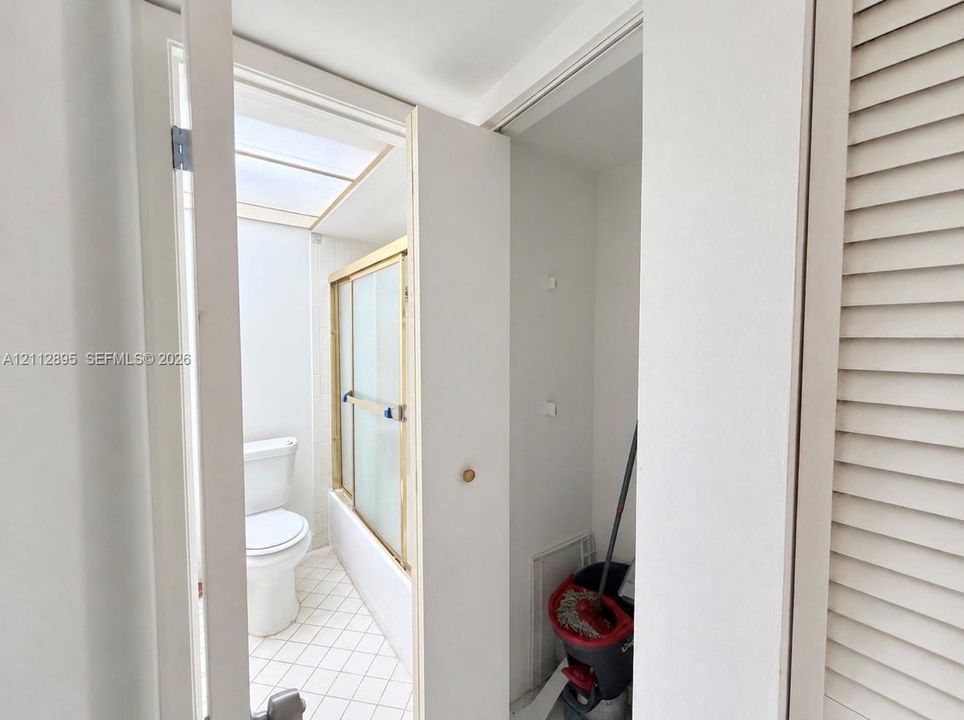 Bathroom featuring a skylight, a shower-tub combination with a metal-framed enclosure, a standard white toilet, and tile flooring