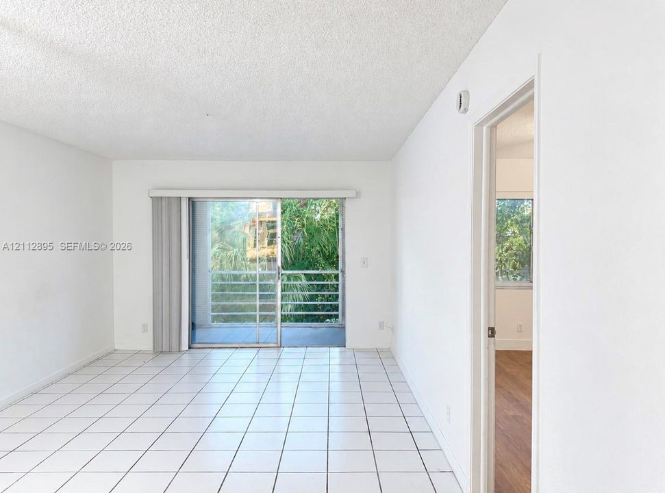 Interior space featuring ceramic tile flooring, neutral white walls, and a glass sliding door opening to a private balcony with metal railing