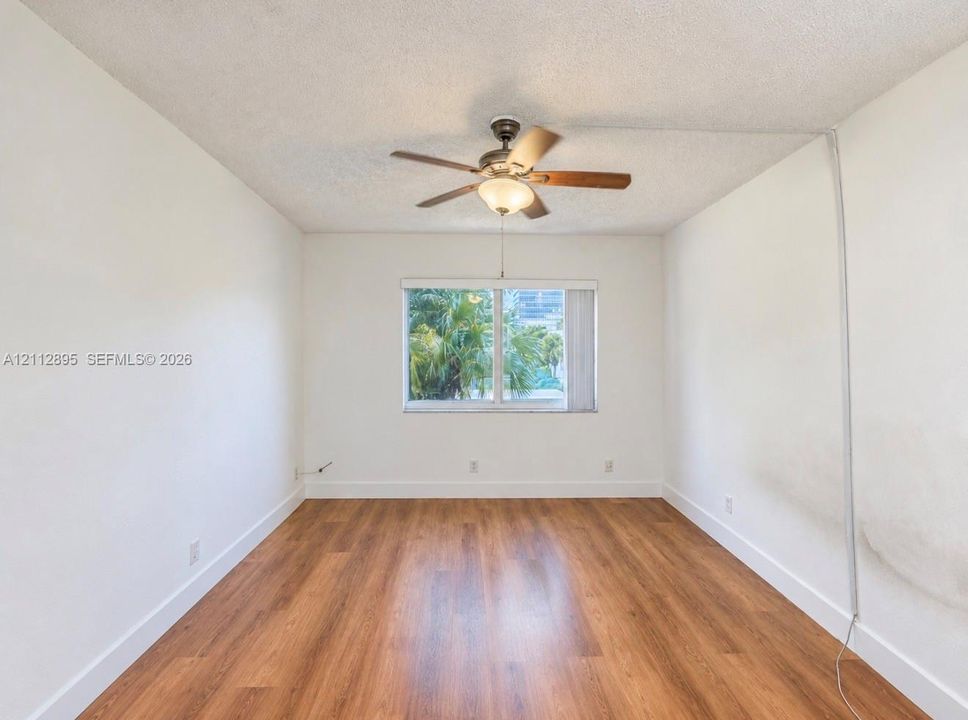 Interior space featuring wood-finish flooring, a neutral color palette, a ceiling fan with integrated lighting, and a window with exterior foliage